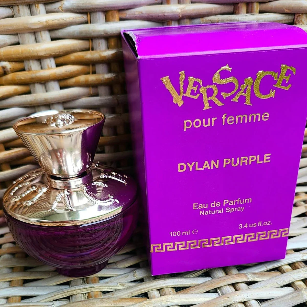 Versace Dylan Purple Eau de Parfum bottle and packaging on a woven surface