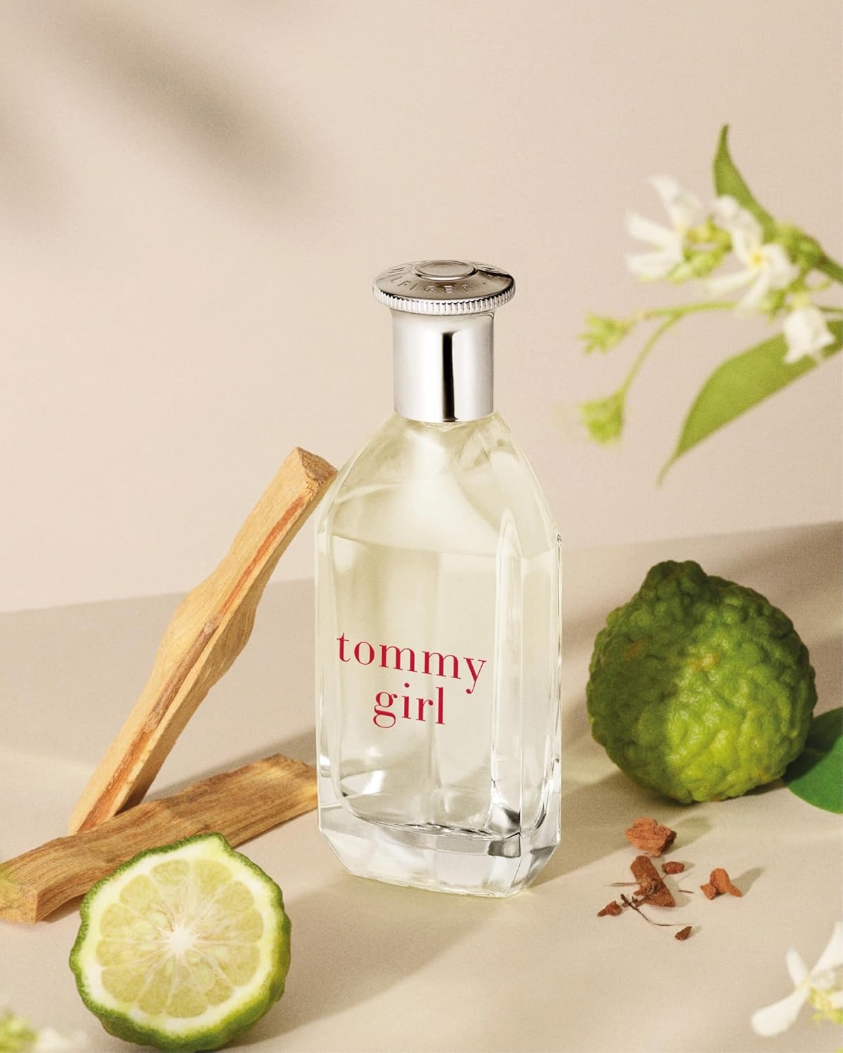 Tommy Girl perfume bottle with lime, lemon, and flowers on a beige background