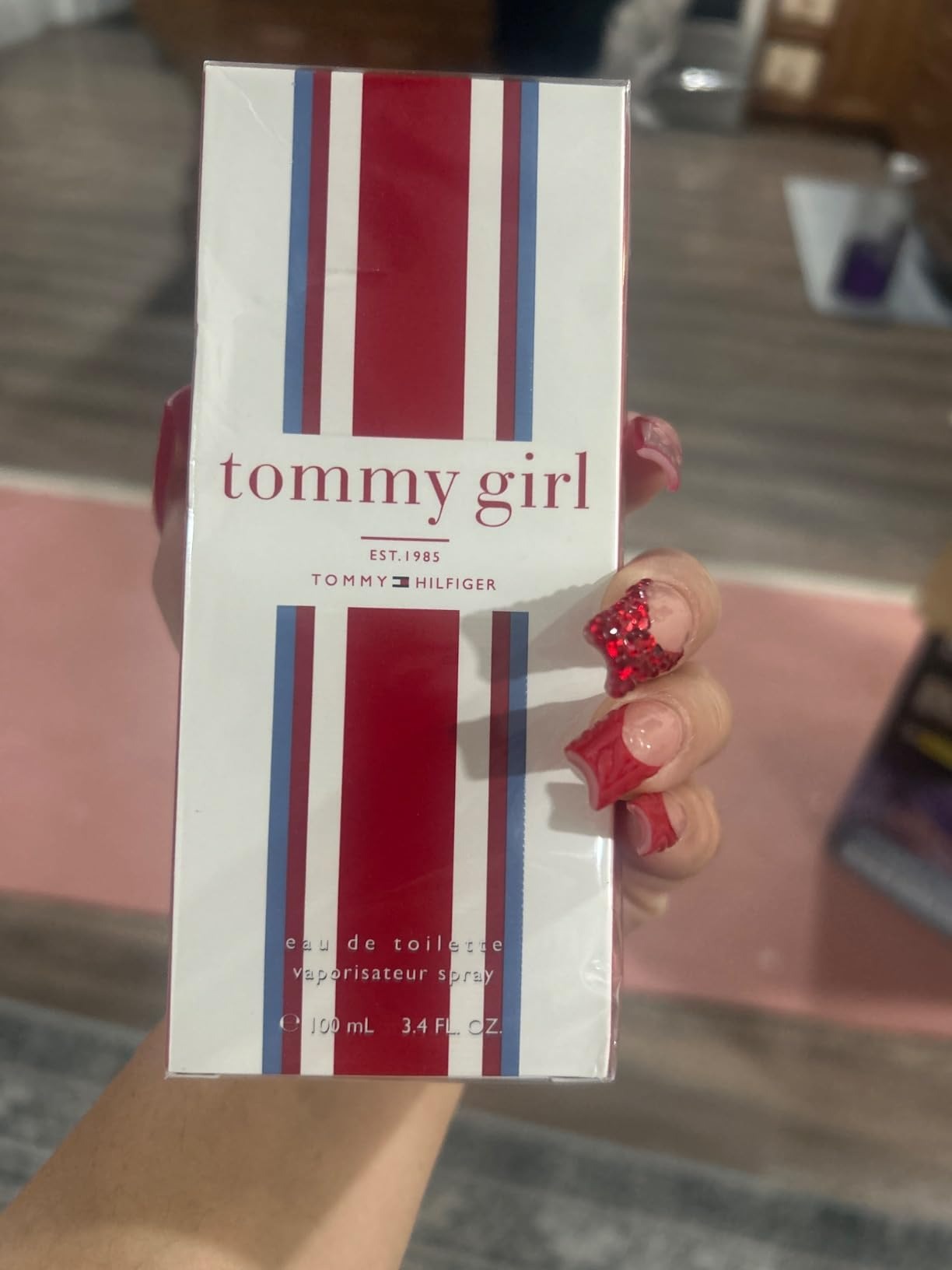 Tommy Girl perfume box held by a person with red nail polish.