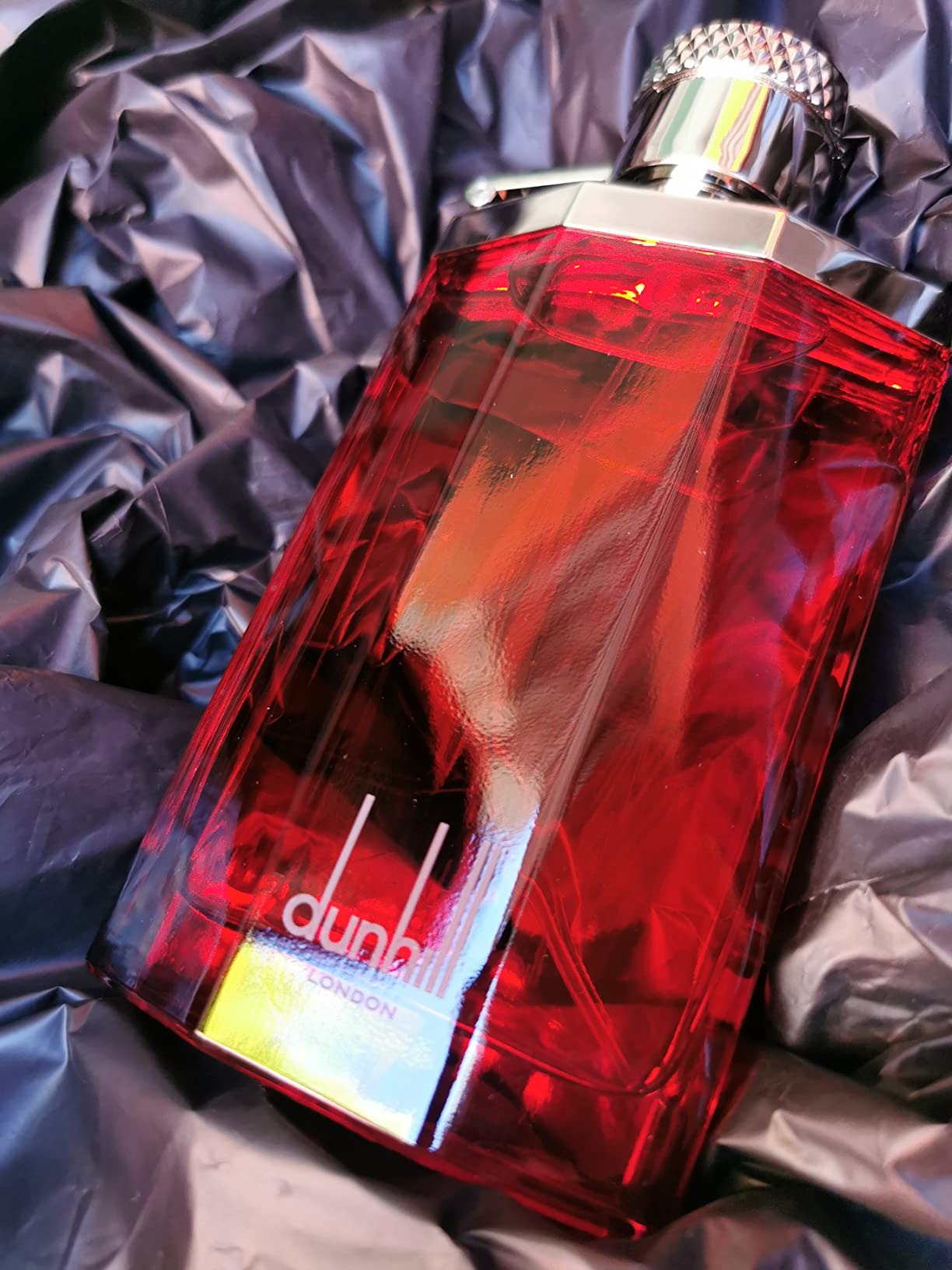 Red perfume bottle with silver cap on a textured gray background